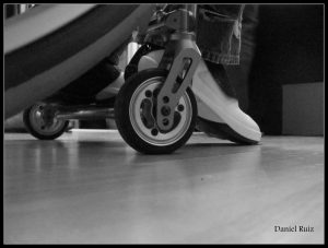 Danny Ruiz--floor view of wheelchair wheels and side of foot in sneaker.