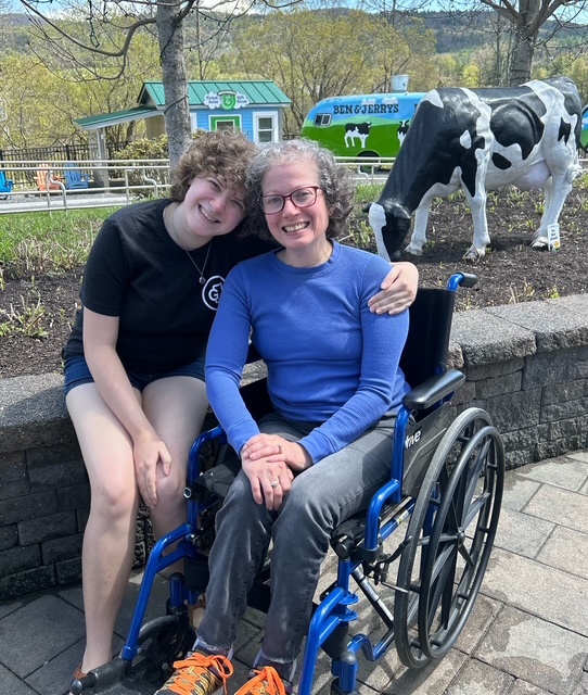 Two white females. The one on the left is embracing her mom on the right. Amy is the one sitting in the wheelchair on the right. 