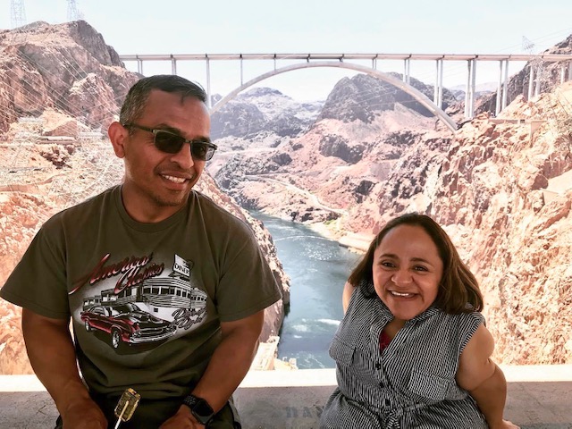 A latino couple poses for the camera with a bridge behind them in the setting. Claudia's faith in God is her reason for this amazing marriage.