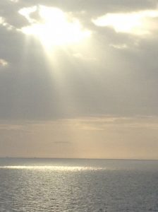 Sunshine streaming through holes in the clouds down to ocean waters.