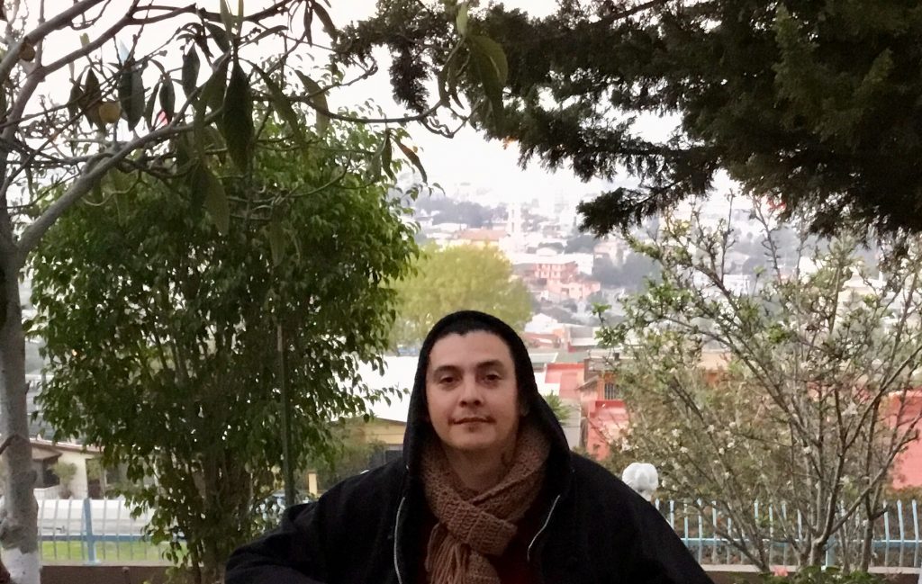 A Latino male looking straight ahead into the camera with a black hoodie on him.