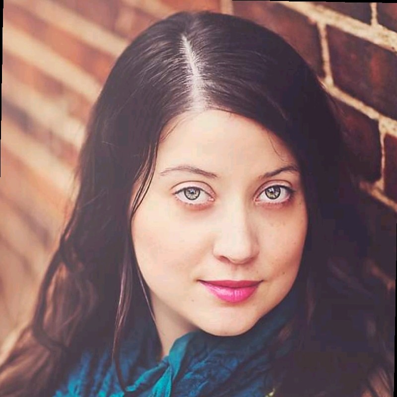 Rachel's headshot. She's staring at the camera. Brunette with colored eyes.