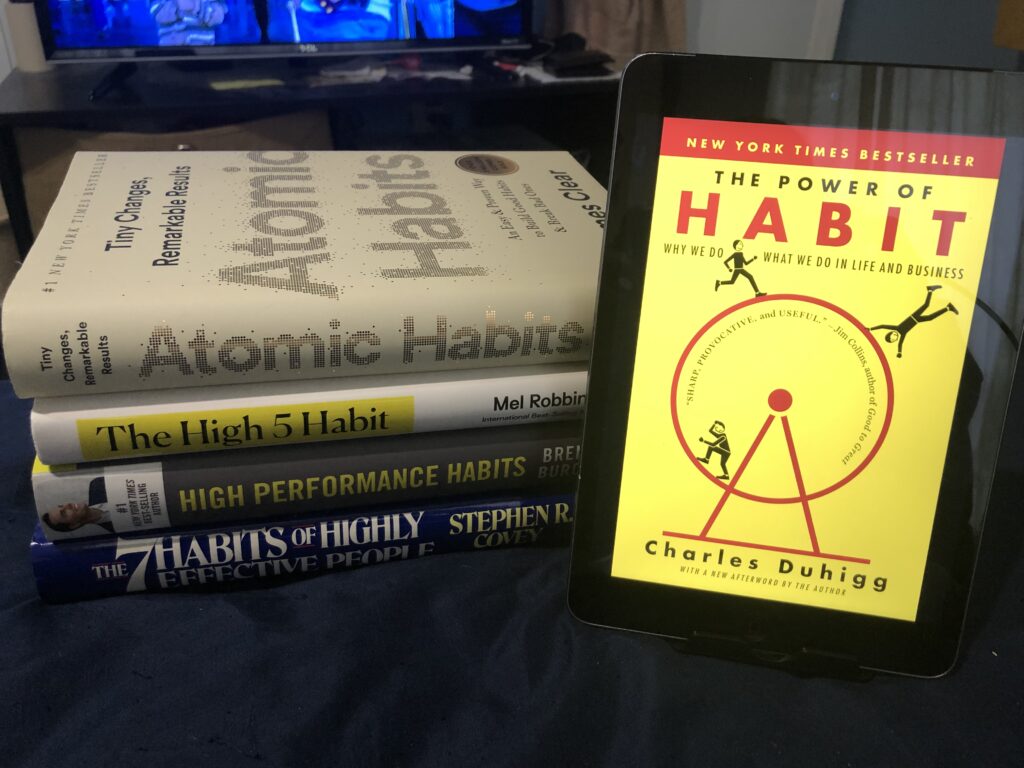 Self Development books stacked up and a book on habits on an ipad