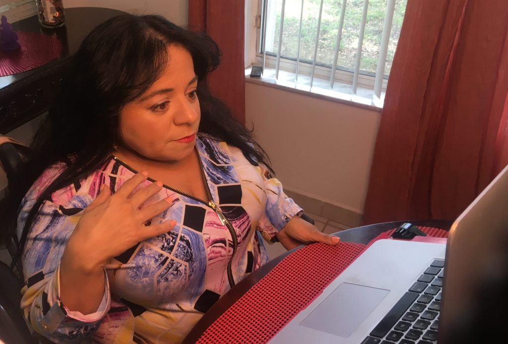Opportunities online Tasha is wearing a multicolored pastel v neck blouse. Latina with dark brown wavy hair parted down the middle. She is staring a laptop. Her right wrist is bending towards her face. She looks pensive.