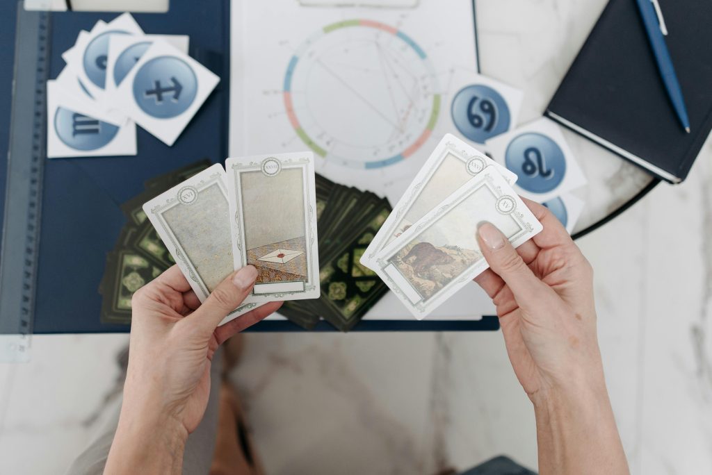 bird's view of two white hands holding tarot cards over a table with an astrological chart