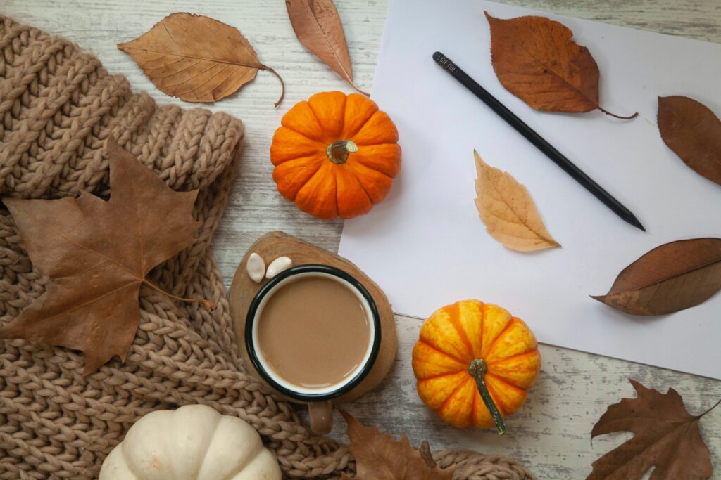 bird's eye view of brown cable knit sweater with a mug of hot cocoa, three small pumpkins, and autumn leaves scattered about. 