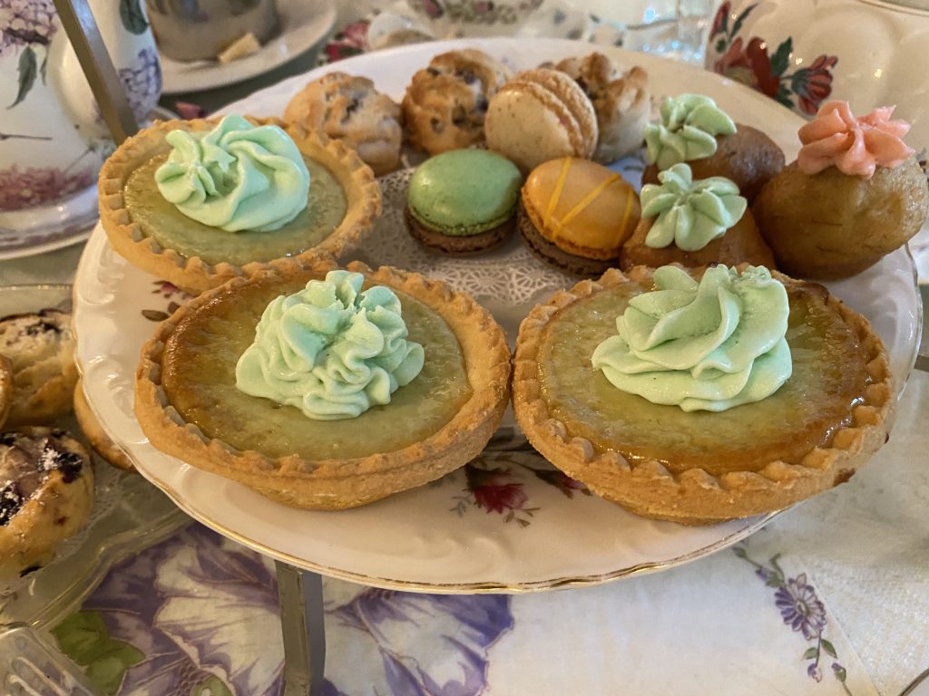 A plate used for tea parties is topped with three mini lime tarts, macaroons, and mini muffins.