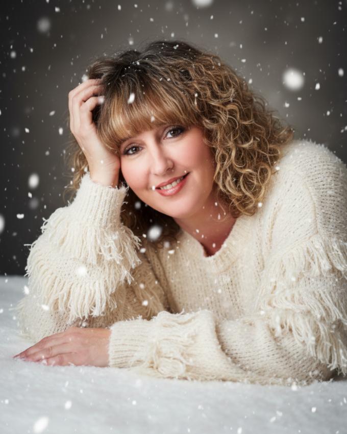 a young woman lying on her side with her right hand holding her head for a fun pose. She is wearing a white knit pullover sweater.