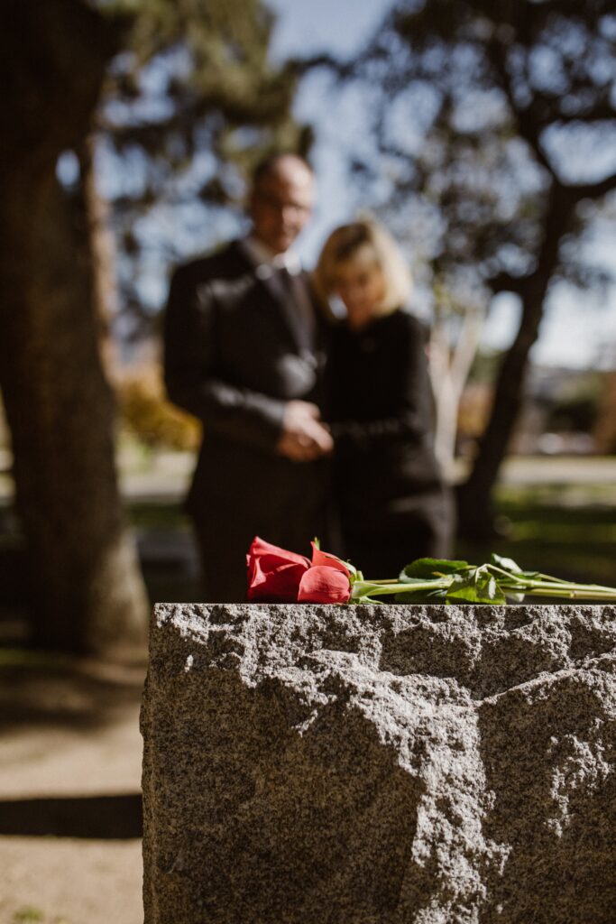 two blurry images, female and male staring at a tombstone with a red rose on top.