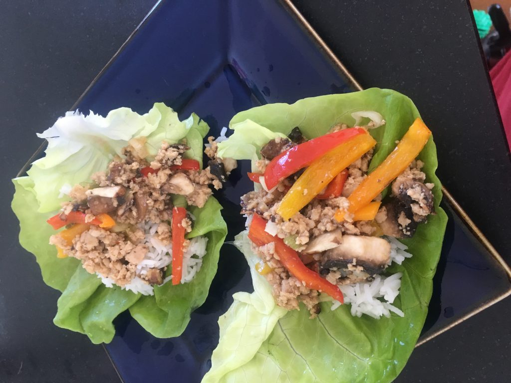 two butter lettuce leaves on a midnight blue dinner plate. Each leaf is topped with rice, ground turkey, mushrooms, and sliced peppers