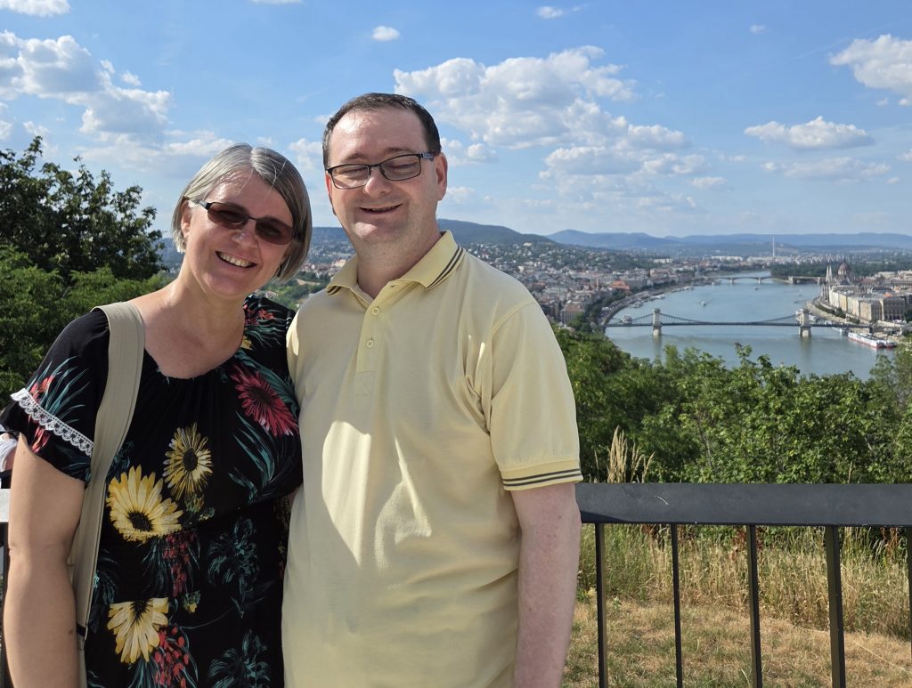 A white female and male Hungarian couple posing in front of The Chain Bridge in Budapest.