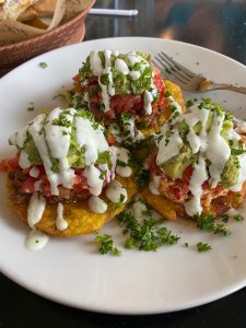 Three tostones with ground beef, diced tomatoes and a white sauce over them. 