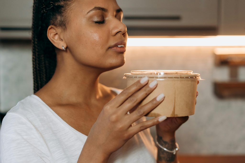 a Black woman smelling a container that appears to be a candle or diffuser