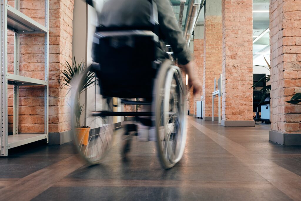 the back of a manual wheelchair rolling away with a person in it. The wheelchair is blurry as if in motion. 
